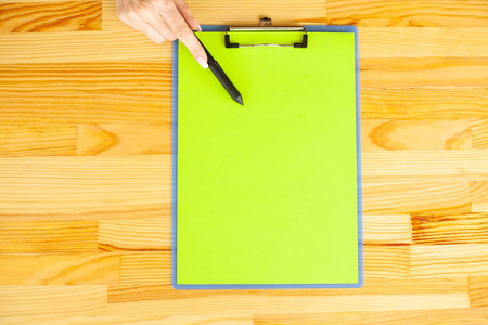 办公室手拿着一个带绿色纸和钢笔的文件夹在木桌的背景上。Copyspace。文本位置