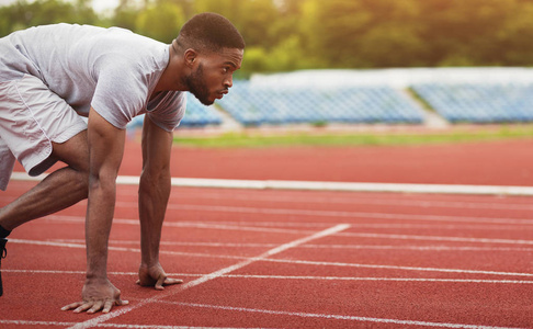 非洲裔美国男性运动员准备在体育场跑道上奔跑