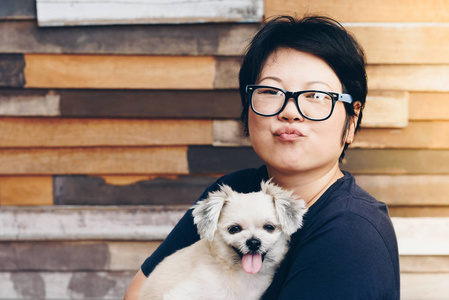 亚洲妇女和狗愉快的微笑拥抱她帕特是一只狗如此可爱混合品种与石慈, 波美拉尼亚和贵宾犬与木木板背景与复制空间