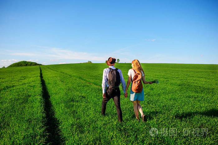 有了背包戴着帽子的男人和长头发的女人沿着小路走一对夫妇沿着草地