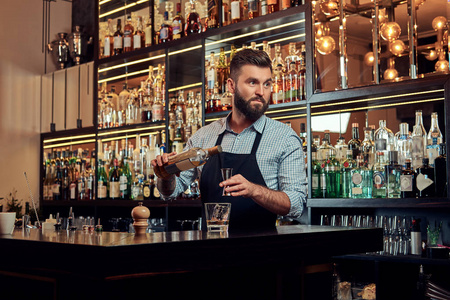 时尚野蛮的酒保在衬衫和围裙做鸡尾酒在酒吧柜台背景照片