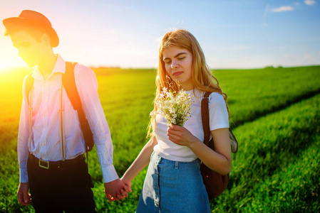 一对恋人把手放在一块绿色的田野上。迷人的男人和一个美丽的女人走在草地之间