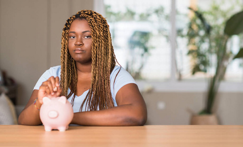 非洲裔美国妇女存钱与小猪银行自信的表情对聪明的脸认真思考