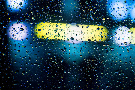 关闭在一个汽车玻璃与一丛雨, 在背景明亮的蓝色和黄色发光灯