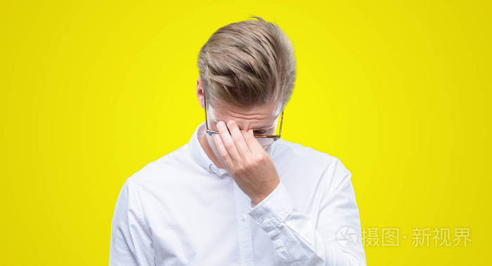 年轻英俊的金发男人疲倦地揉鼻子和眼睛感到疲倦和头疼.