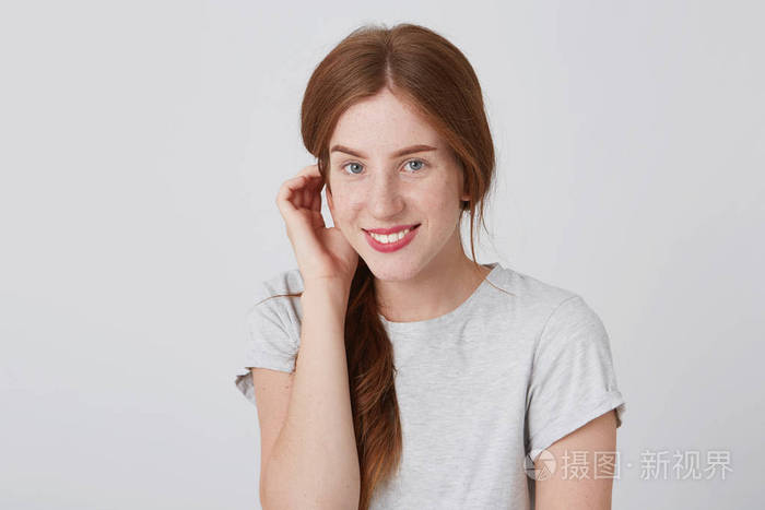 微笑可爱的红头发的年轻女人的肖像抚摸她的头发, 看着相机隔离在白色