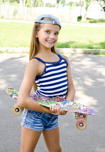 可爱的快乐微笑的小女孩与滑板户外在夏天的一天