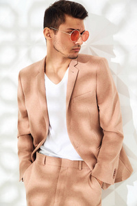 时尚时尚的 lumbersexual 模特身着优雅的淡粉色西装, 在演播室的白色墙壁附近。型男