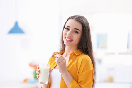 美丽的年轻妇女喝牛奶与饼干在家中