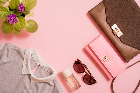 设置衣服, 钱包和袋子, 梳子和太阳镜, 自粘和香水。花在粉红色的背景旁边。女性夏季流行趋势