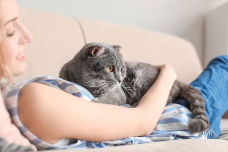 家庭沙发上的年轻女子与她可爱的宠物猫