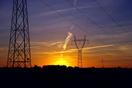 日落时的电塔剪影。橙色天空中的高压能量线