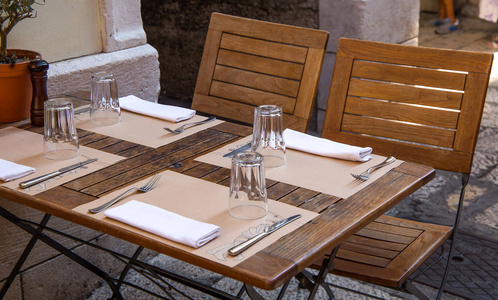 眼镜, 叉子, 小刀, 餐巾在棕色的木桌上, 在外面的舒适餐厅吃午饭。