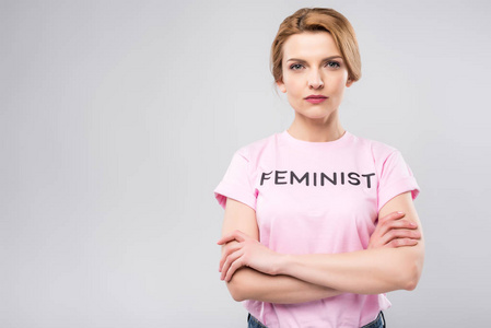 自信的女人在粉红色主义的 t恤与交叉的武器, 孤立的灰色