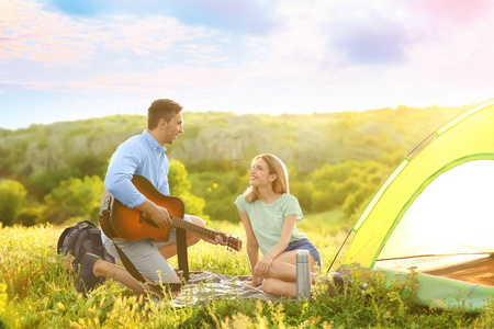 年轻人在荒野露营帐篷附近为女友弹吉他