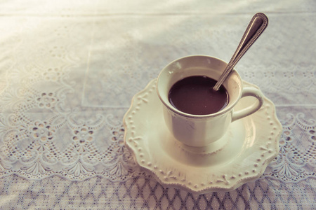 带热咖啡的白杯子和早晨的休息时间在一个漂亮的图案布的桌子上