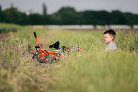 田野里的男孩坐在自行车旁边。