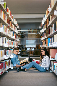 在大学图书馆学习的学生。男人和女人看书坐在书架之间的地板上。高分辨率