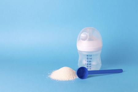 儿童的干混合饲料, 测量勺, 喂养瓶与奶嘴在蓝色的背景。人工喂养的概念