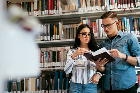 大学图书馆的几个学生。男人和女人在书架附近看书。高分辨率