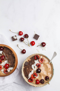 巧克力樱桃冰沙碗与椰子和香蕉在白色背景, 顶部视图。健康的素食观念。纯素食生活方式