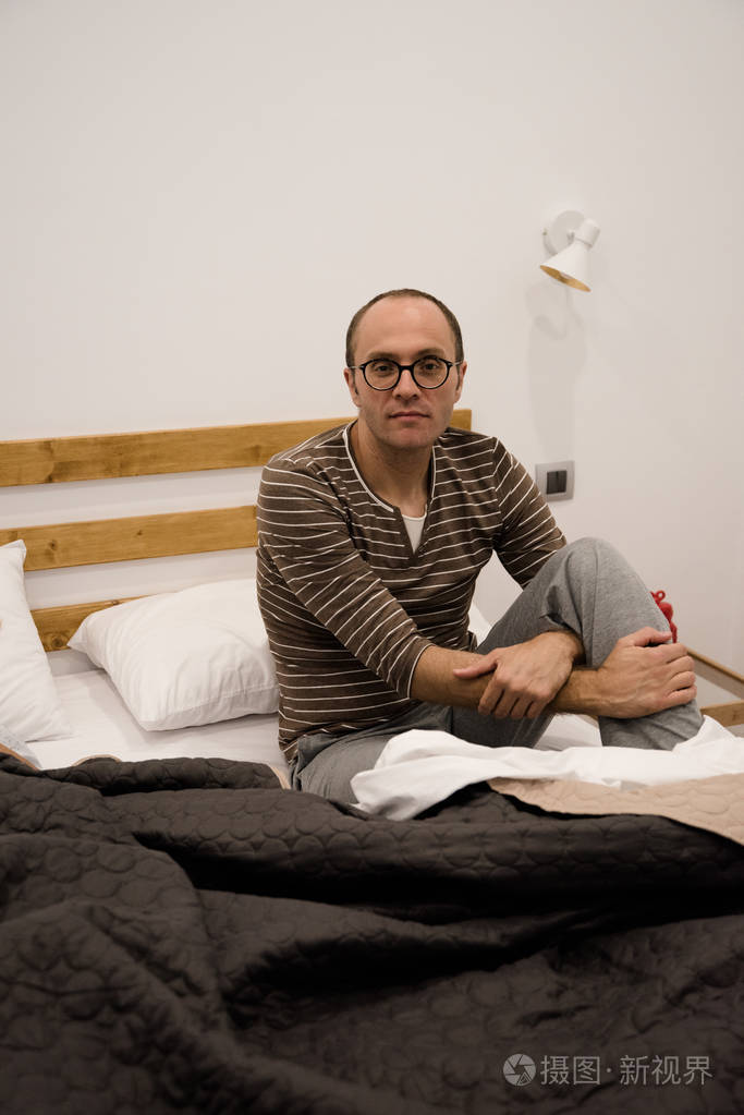 男子坐在卧室的床上他的腿交叉看着相机