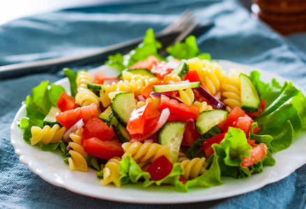 蔬菜面食沙拉配番茄, 生菜, 洋葱和黄瓜在桌上的白盘子里