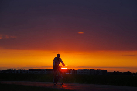 人的剪影在自行车与城市和尼斯日落在背景