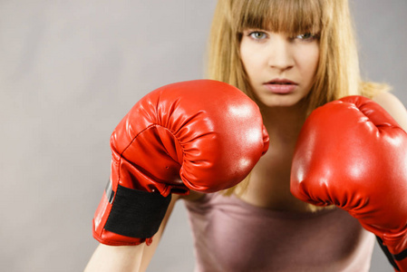 运动型女人戴着红色的拳击手套，战斗。工作室拍摄灰色背景
