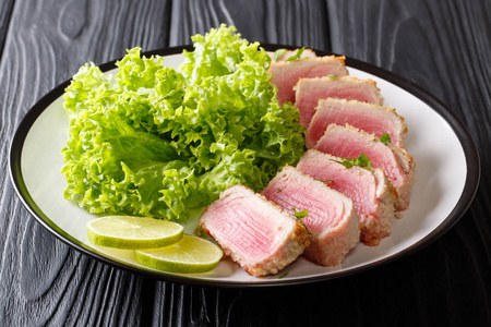 美味的金枪鱼牛排煎在育种与叶沙拉和石灰特写在一个盘子上的黑色桌子上。horizonta