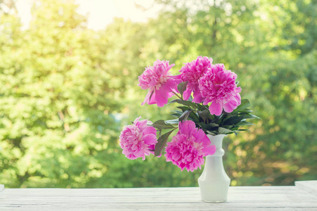 美丽的淡粉色牡丹花束在白色花瓶在自然绿色背景