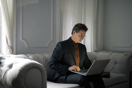 商人坐在沙发上, 并与他的电脑在一个优雅的内部工作