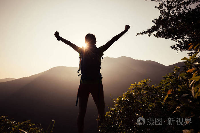 成功的女性徒步旅行者与 outstreched 胳膊站立在山顶在日出期间