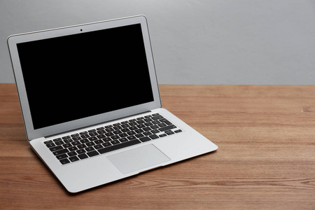 带空白屏幕的现代笔记本电脑在灰色背景下的木桌