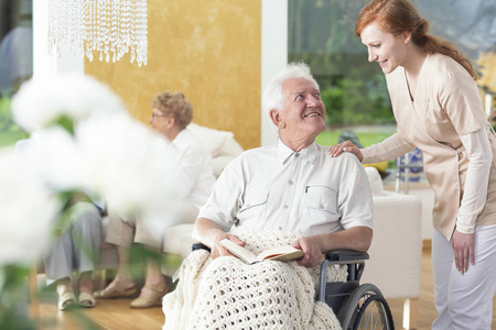 一个年老的男人在一个康复中心的休息室里和一个私人助理说话