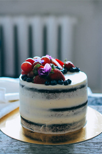 巧克力蛋糕与奶油奶油装饰草莓, 蓝莓, 葡萄和紫罗兰在一个木质的背景