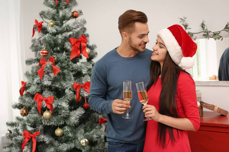 年轻美丽的夫妇与香槟杯在家里的圣诞树附近