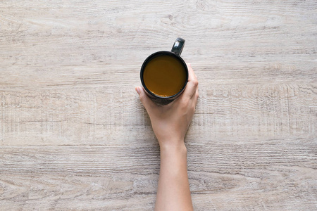 女性手捧一杯咖啡在木质纹理背景上