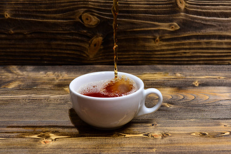 杯子倒有溅水和水滴的液体。酿造茶的概念。杯浇水或茶与溅在黑暗的木质背景。木桌上的杯子和泡茶