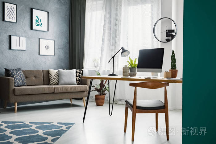 在客厅的办公桌上的木椅, 里面有工作区和灰色墙上的海报.真实照片