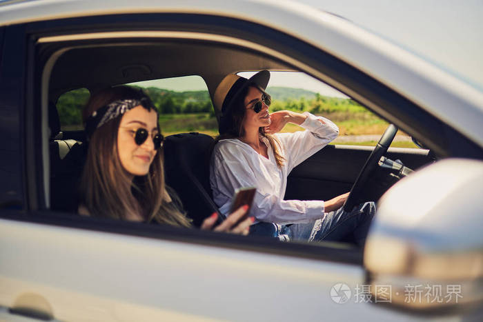 两个女孩在车里开车一个女孩驾驶和其他使用智能手机短信