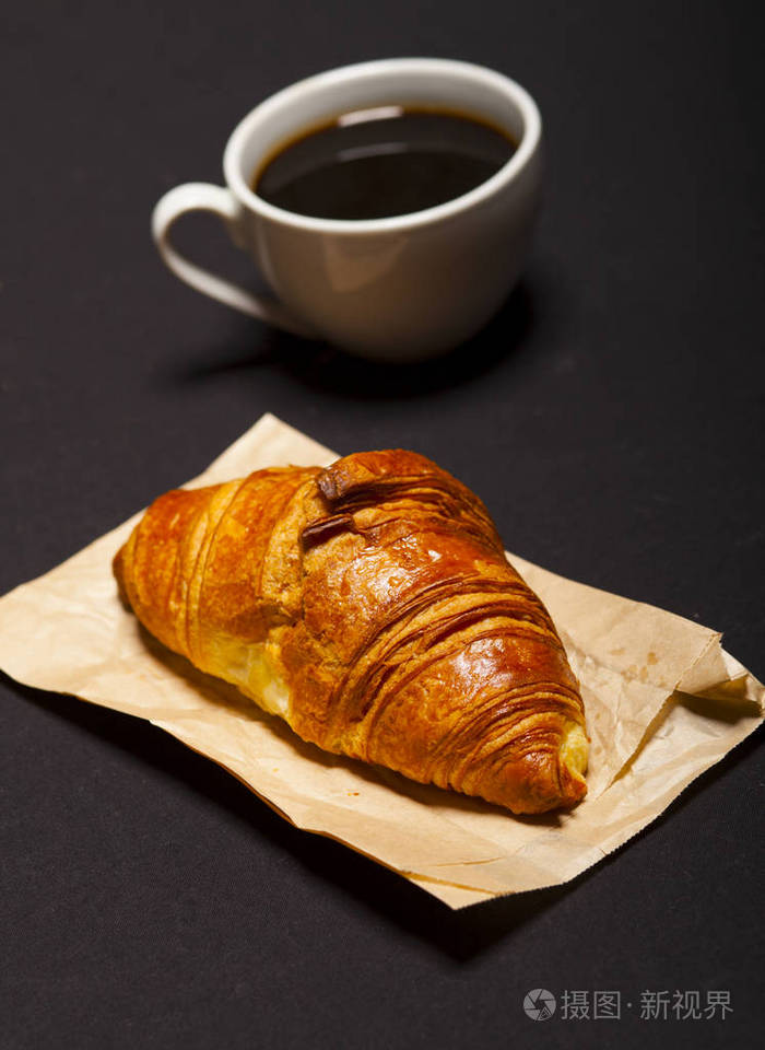 在黑色背景下的羊角面包和咖啡杯