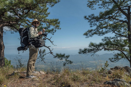 摄影师与专业相机在山顶上。登山者爬上雾谷上方的岩石峰