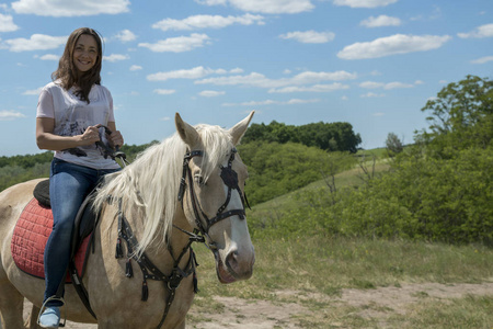 夏天田野上一匹大马的小妇人的照片。快乐女性的形象坐在纯种马和看在室外摄像机
