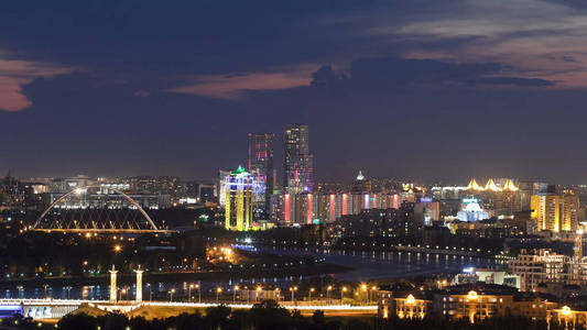 在市中心和中央商业区的高的夜看法与桥梁和河 Timelapse 从屋顶, 日夜, 当照明打开时, 哈萨克斯坦, 阿斯塔纳, 中亚