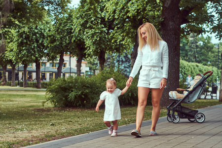 快乐的年轻母亲散步与她的小女儿在公园的人行道上