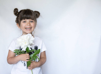 快乐的孩子捧着一束白色的牡丹花, 微笑着。白墙背景, 复制空间