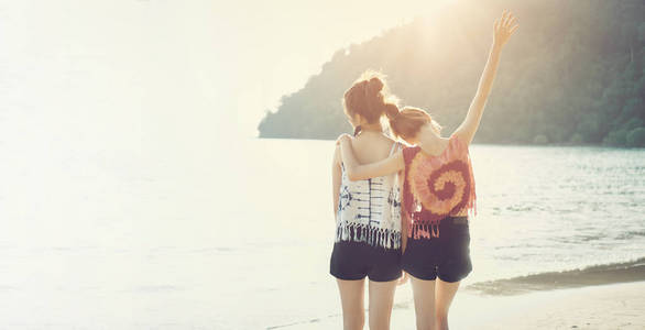 夏天的时候, 两个女孩抱着脖子, 背对着海滩。晚上, 太阳从后面美丽