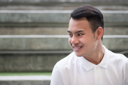 快乐英俊的男人坐在城市环境微笑;具有棕褐色皮肤和短发的年轻成 