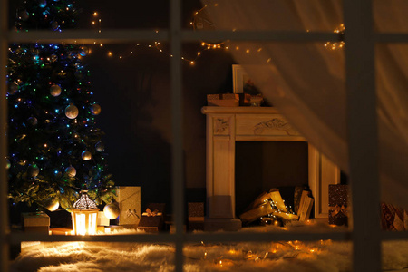 时尚客厅内饰装饰圣诞树和壁炉在晚上, 通过窗口查看